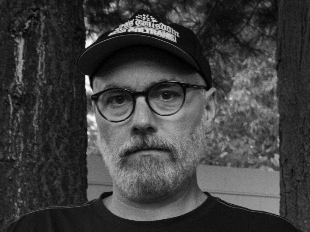 TW Walsh, in a baseball cap and round glasses, among trees.